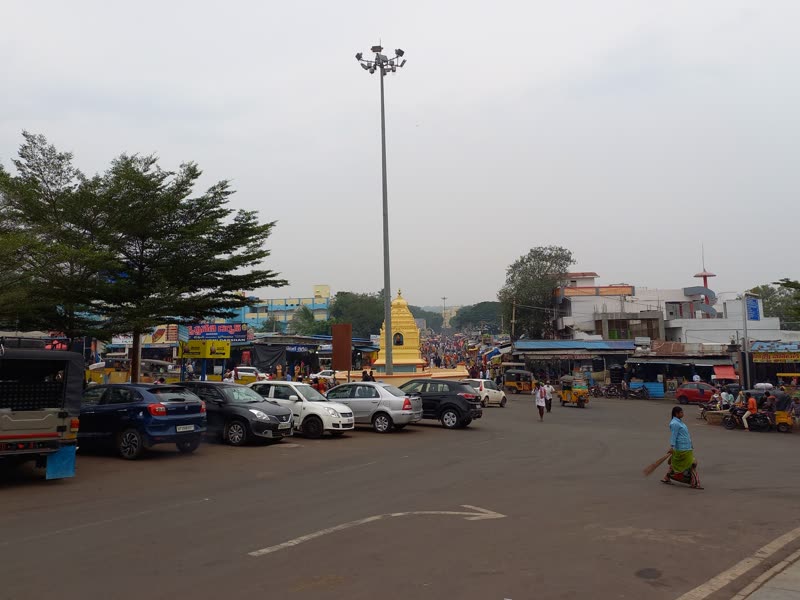A busy town street with parked cars and shops in Srisailam